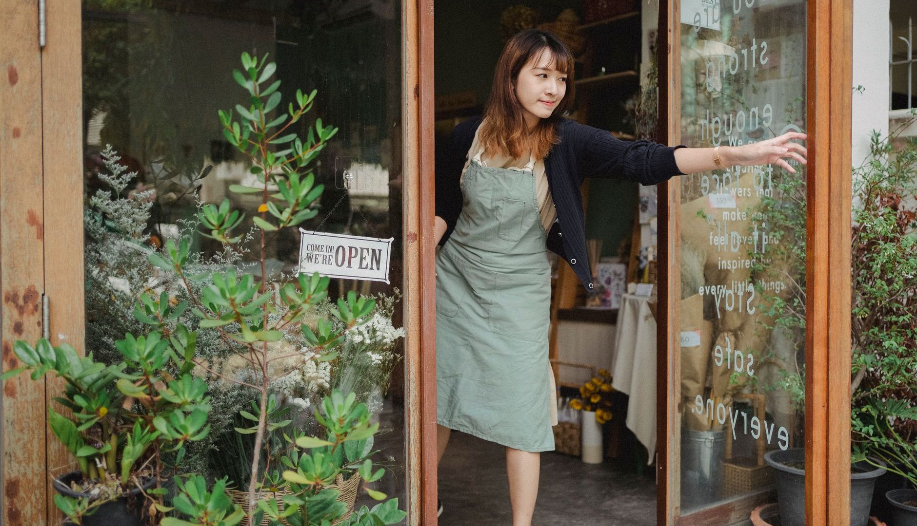 fleuriste ouvrant la porte vitrée de sa boutique, panneau ouvert accroché à la vitrine