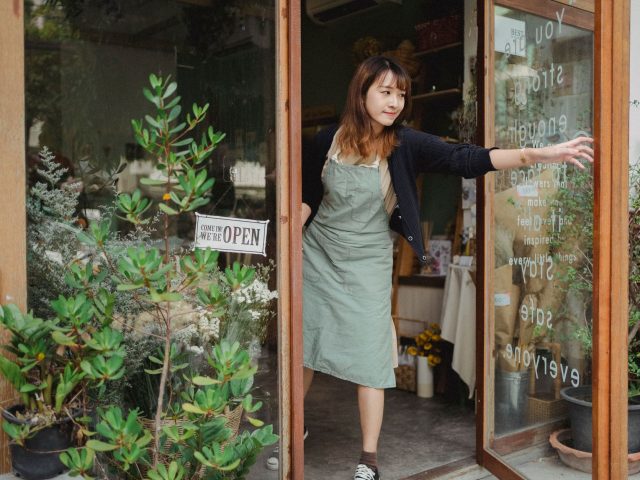 fleuriste ouvrant la porte vitrée de sa boutique, panneau ouvert accroché à la vitrine