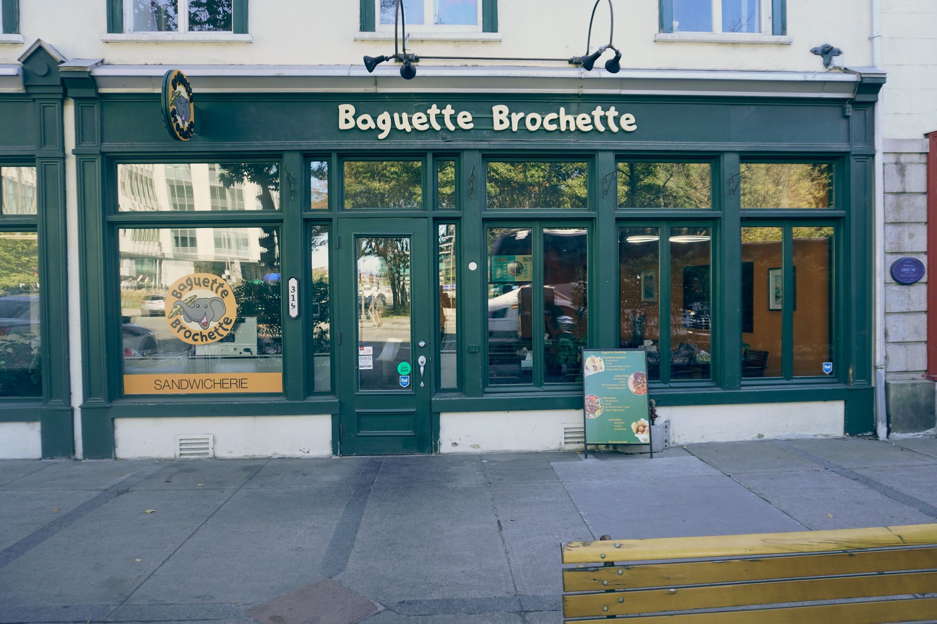 façade verte d'une sandwicherie avec enseigne en lettres découpées, logo en vitrine et chevalet menu sur le trottoir