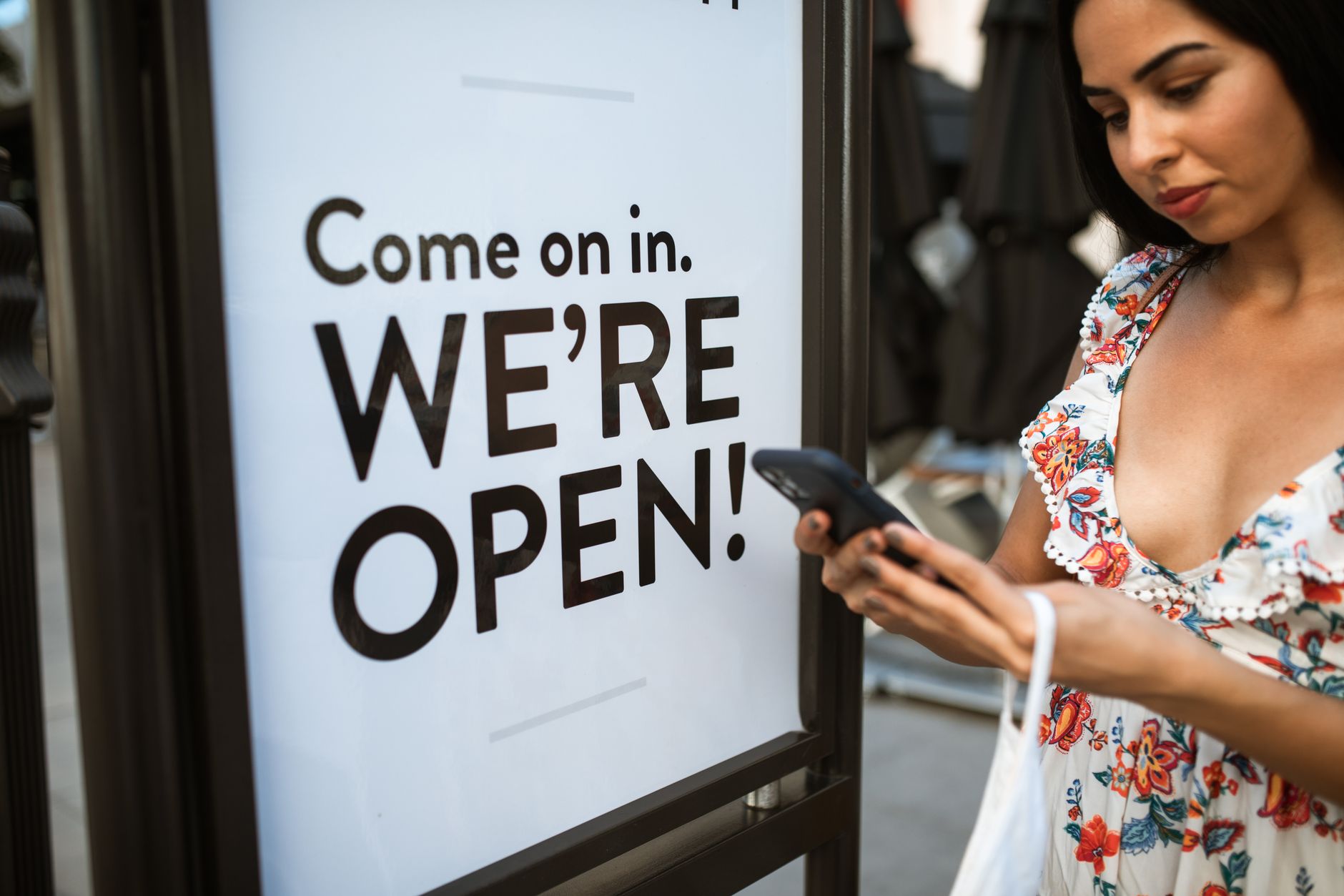 femme consultant son téléphone devant un panneau indiquant qu'un commerce est ouvert