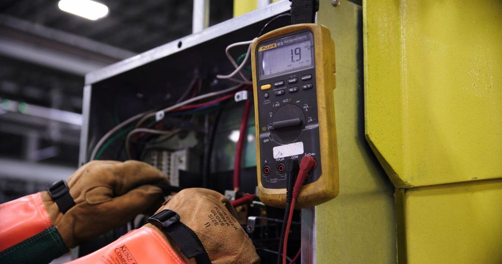 Électricien utilisant un multimètre pour vérifier un tableau de contrôle industriel