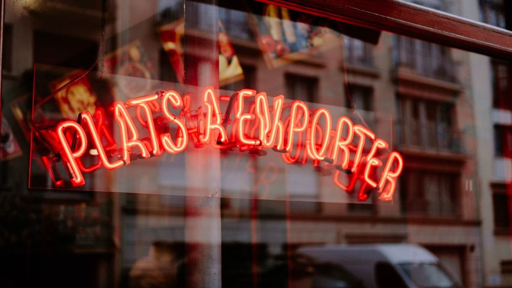 Enseigne néon rouge Plats à Emporter reflétée dans une vitrine de nuit