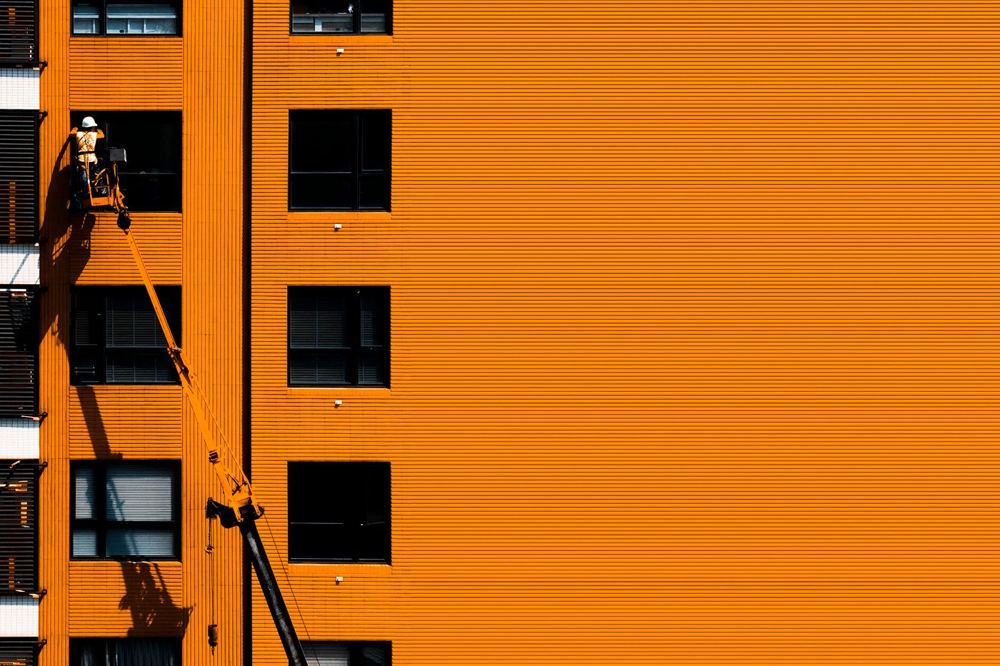 Ouvrier du bâtiment en nacelle sur une façade orange