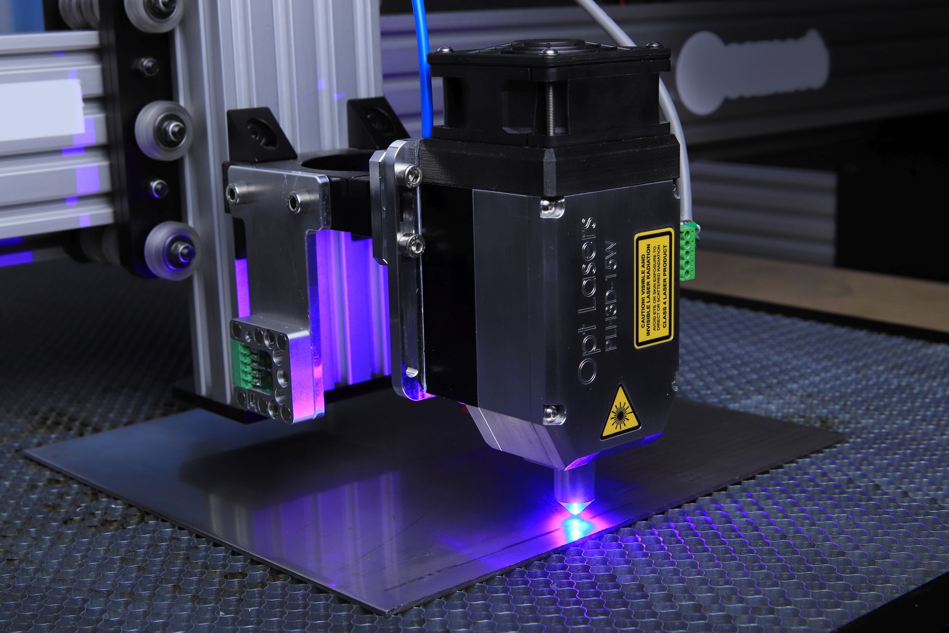 tête de gravure laser au travail au-dessus d'une plaque métallique, lumière bleue au point de contact