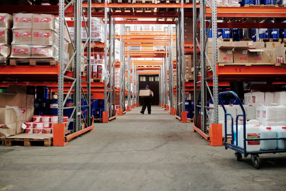 Employé transportant un carton dans une allée d’entrepôt bien rangé