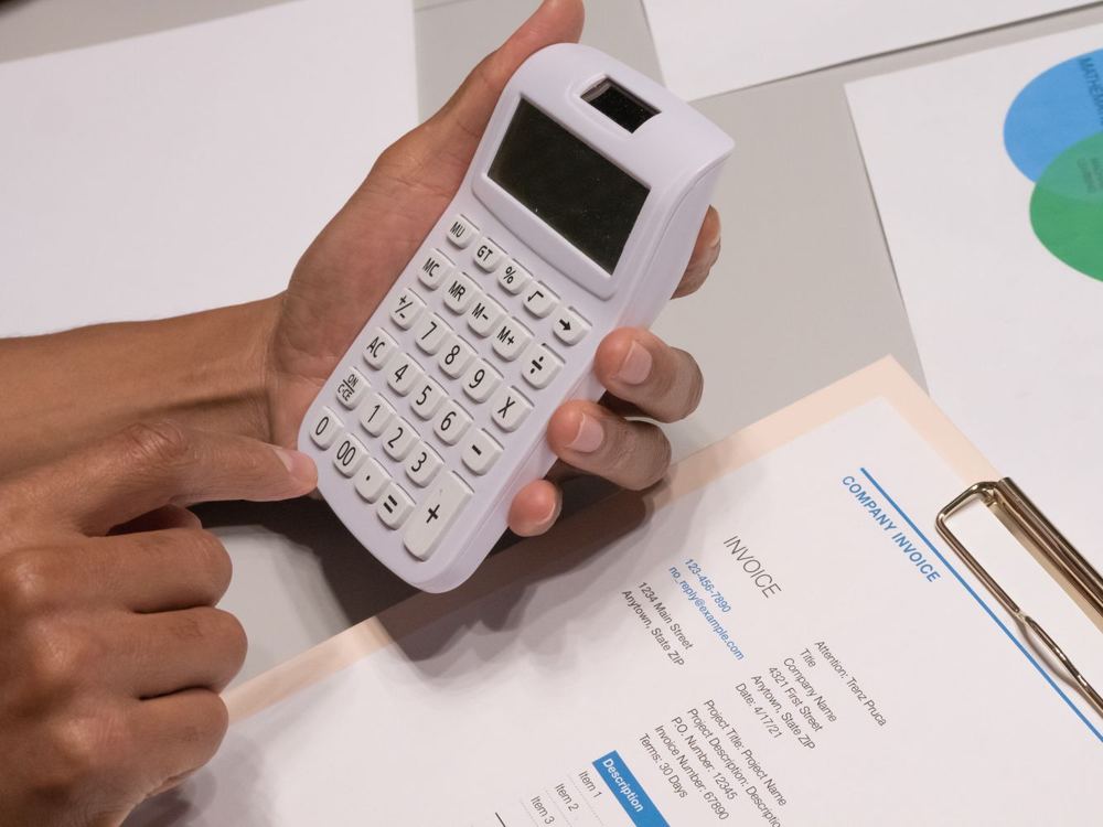 Mains utilisant une calculatrice à côté d’une facture d’entreprise