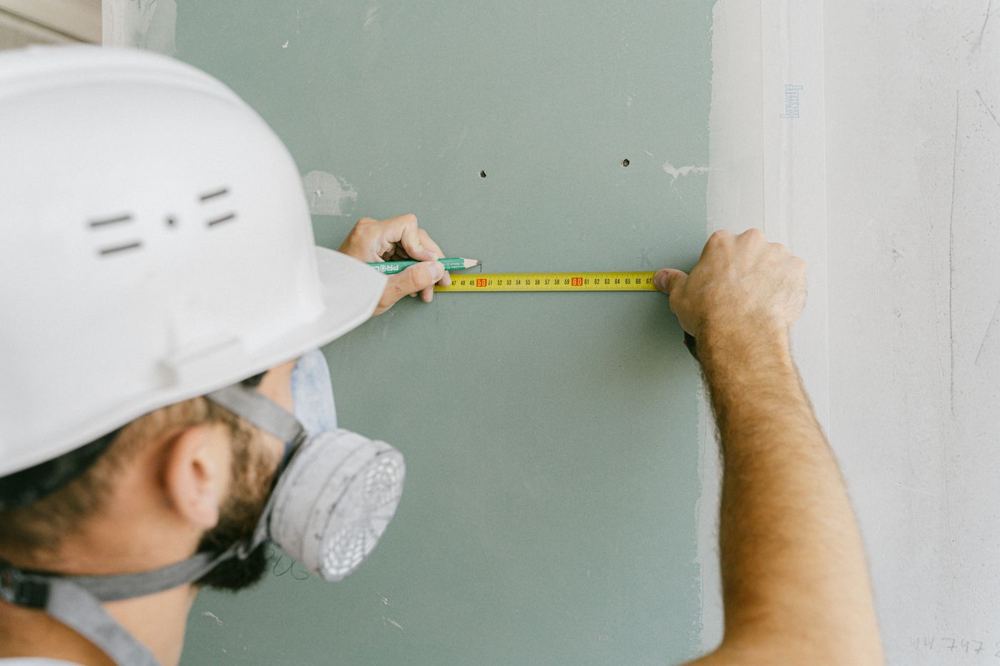 Ouvrier du bâtiment mesurant une surface avec un mètre ruban