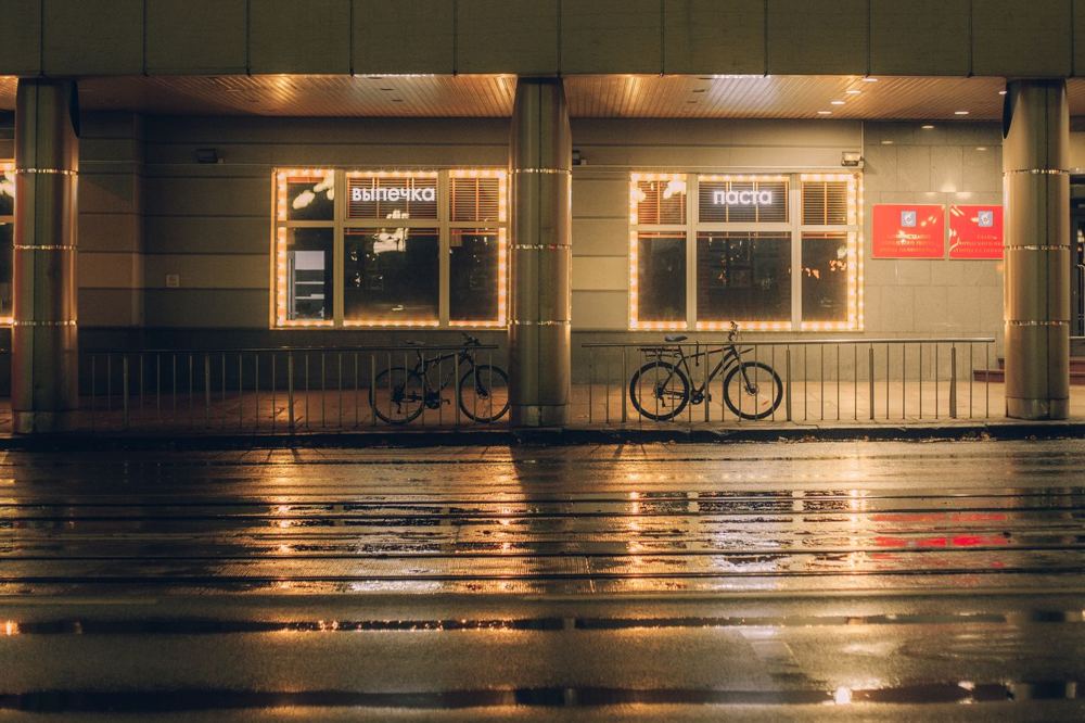 Scène urbaine nocturne avec vitrine commerciale éclairée et reflets sur chaussée mouillée