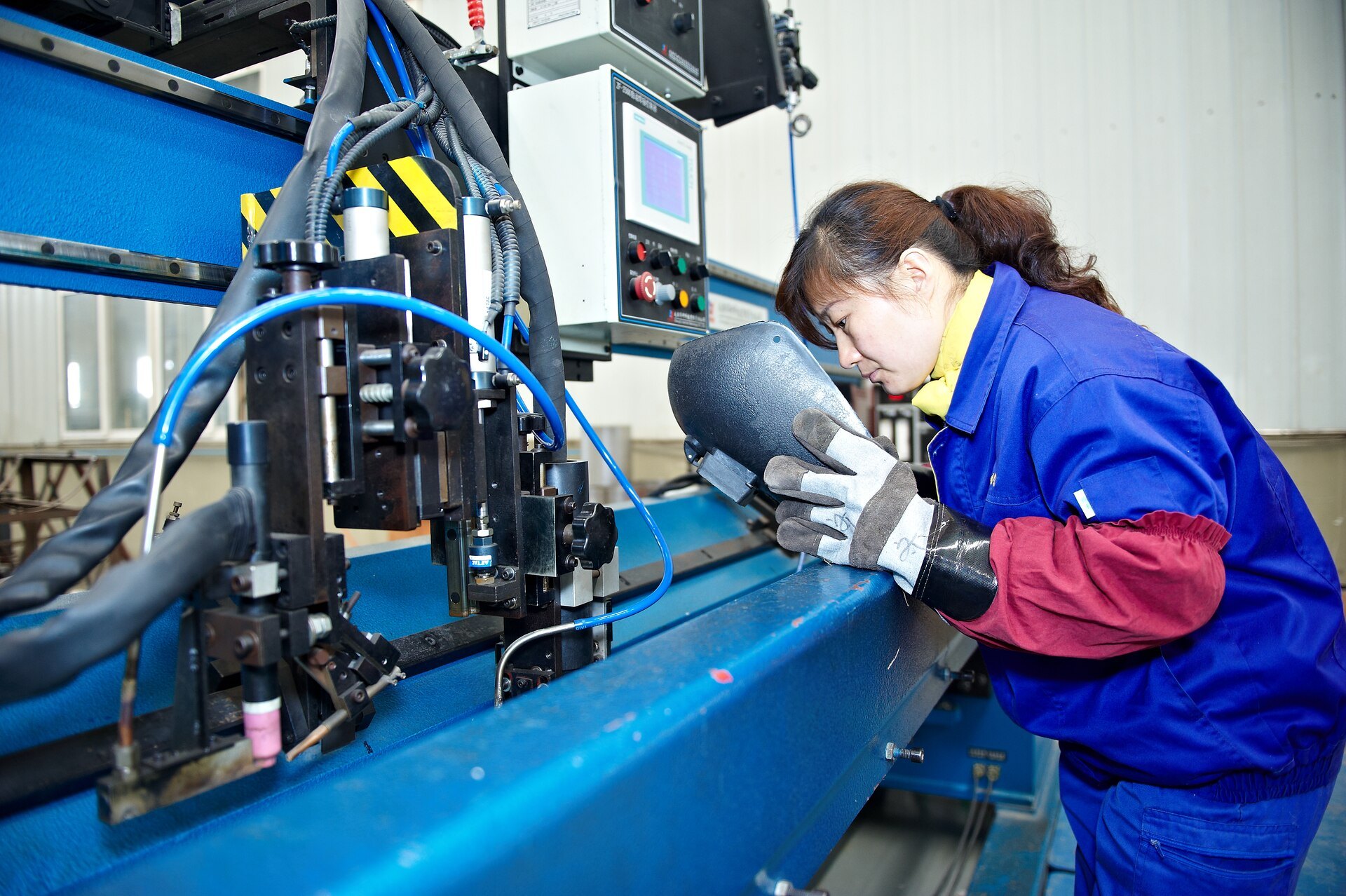 opératrice en tenue de protection penchée sur un poste de soudage laser automatisé en atelier